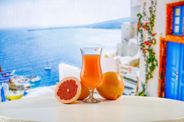 Glass of citrus fruit juice and fruit on a wooden table against the backdrop of the blur white buildings. The sunlight and a summer background with space for food and drink and a product.