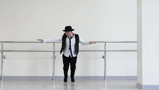 Rhythmic dance cha cha or bachata. Handsome young dancer in creative jazz clothes. Street Dancer in a hat with a tie and a black vest and jazz shoes, against the background of a wall.