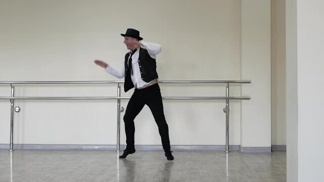 Rhythmic dance cha cha or bachata. Handsome young dancer in creative jazz clothes. Street Dancer in a hat with a tie and a black vest and jazz shoes, against the background of a wall.