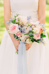 A bride is holding a summer pink summer bouquet with blue ribbon. 