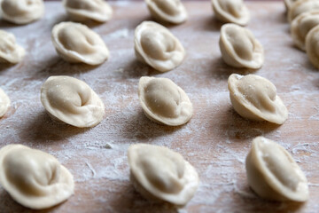 The raw dumplings were placed on a wooden cooking board, sprinkled with flour. The filling is minced meat, potatoes, cheese or cottage cheese. A semi-finished product, ready for cooking.