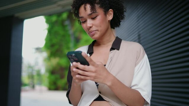 young woman stands outdoors, focused on smartphone while engaging in digital conversation. Female feeling contentment, enjoying moment interacting online in chat. modern, connected lifestyle
