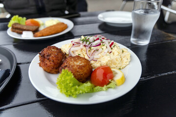 Seafood restaurant on the seashore. White plate with fish patties, fish fillets and potato salad.