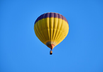 A vibrant yellow hot air balloon floats gracefully in a clear blue sky, offering a sense of adventure and freedom.