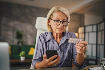 Mature woman hold the medicine and read instructions on mobile phone