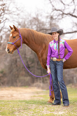 Barrel racer Cowgirl in purple shirt and hat with sorrel Quarter horse 