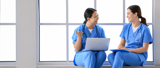 Female Asian doctors with laptop sitting on window sill in clinic