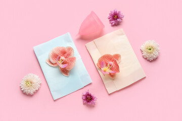 Menstrual cup with pads and flowers on pink background