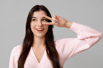 Young woman showing peace sign on light background, closeup