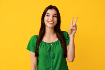 Young woman showing peace sign on yellow background