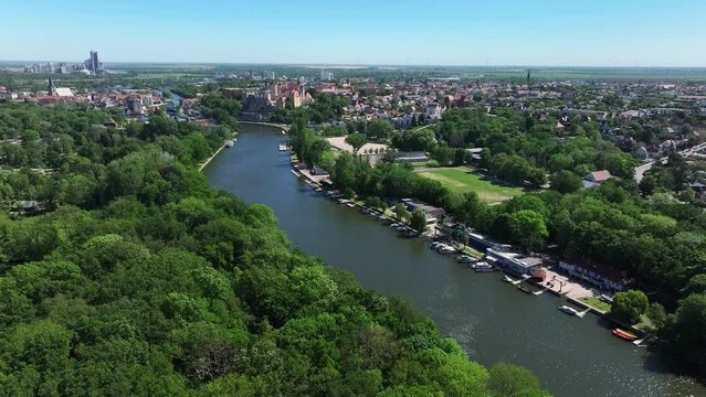 Flight towards the city center of Bernburg along the river Saale. Sports boats are moored on the banks. Beautiful nature in Saxony-Anhalt. The historic city center of Bernburg in the background.
