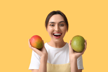 Beautiful young woman with sweet mango fruits on yellow background