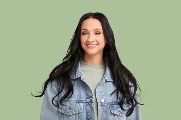Beautiful young woman with dark wavy hair in denim jacket on green background