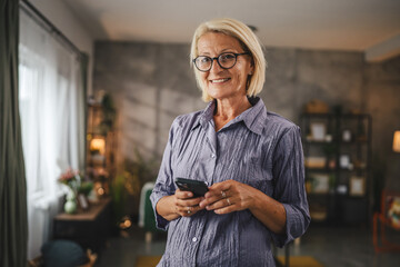 Portrait of mature woman stand and use mobile phone at home