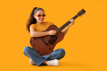Young woman playing guitar on yellow background