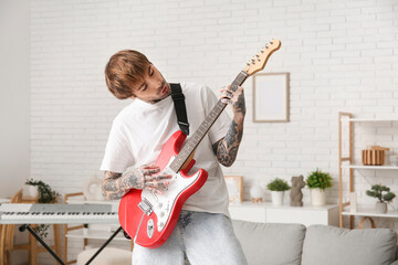 Cool tattooed young man playing electric guitar at home