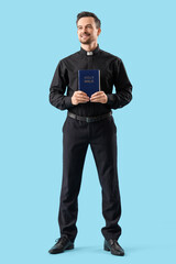Portrait of male priest with holy Bible on blue background