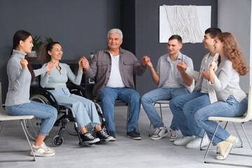 Mature woman in wheelchair with people holding hands at group therapy session