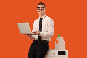 Young businessman using laptop near washing machine on orange background