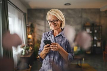 Portrait of mature woman stand and use mobile phone at home