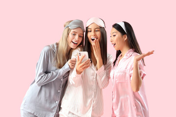 Young women in pajamas using mobile phone on pink background. Hen Party