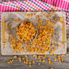 Sultani seedless raisins. Dried Sultani seedless raisins in a copper bowl served on a marble tray, raisins scattered around a copper bowl of raisins.