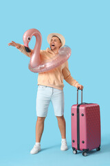 Male tourist with suitcase and inflatable ring pointing at something on blue background