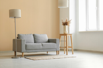 Comfortable grey sofa with lamp and pampas grass in living room