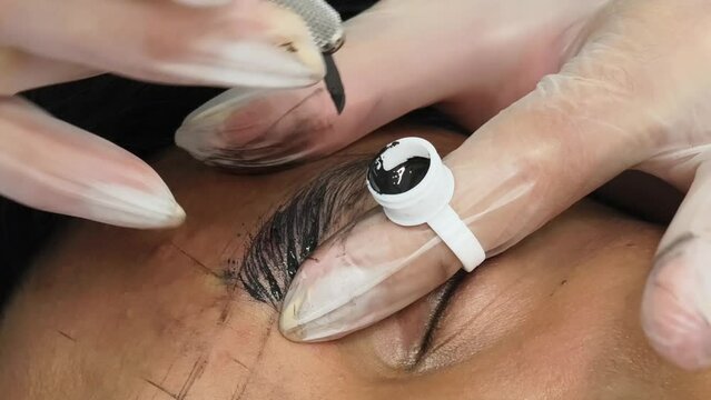 An esthetician using a microblade tool to make small cuts into the eyebrow of a customer. A Microblading technique to implant pigment. Male brow enhancement.