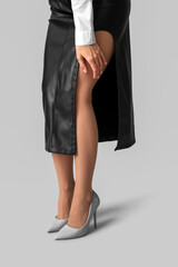 Fototapeta premium Young woman in beige tights and leather skirt on grey background