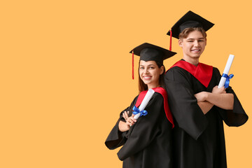 Happy graduate couple with diplomas on yellow background