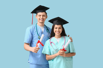 Happy medical graduate couple with diplomas and stethoscopes on blue background