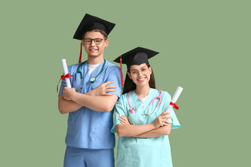 Happy medical graduate couple with diplomas and stethoscopes on green background