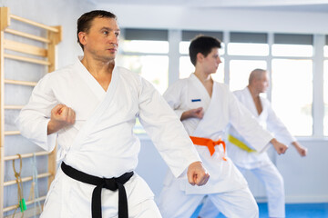 Adult male karateka practicing karate technique in group in gym