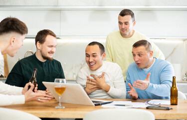 Fototapeta premium Group of joyful friends watching football match on a laptop together and drinking beer