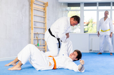 Obraz premium Men train to throw on the mat under the guidance of a judo coach