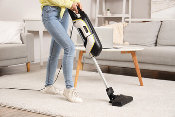 Young woman cleaning carpet with cordless stick vacuum cleaner in living room