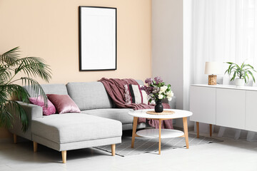 Beautiful living room with bouquet of lilacs branches on coffee table, cozy sofa and cushions