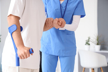 Female physiotherapist helping man with crutch to walk in rehabilitation center, closeup