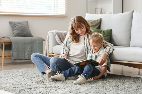 Happy mother and her little son reading book on floor in living room at home