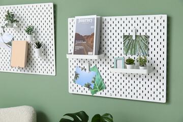 Pegboards with magazines, pictures and houseplants on green wall in living room