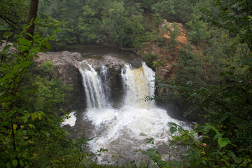 Obraz premium Double Waterfall at Redwood Falls MN with Green Trees Rocky Cliff and Orange Terrain