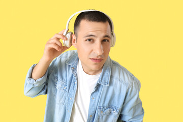 Handsome young suspicious man in headphones on yellow background