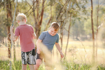 Brothers playing together swinging on rope in the Australian bush
