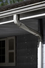 Dark stormy day, rain water overflowing roof gutter and clogged downspout, residential house...
