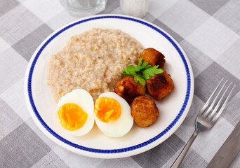 Breakfast is served on table - side dish of oatmeal, portion of meatballs and hard-boiled egg cut in half.