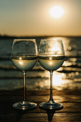 Two glasses of wine on wooden table near river at sunset