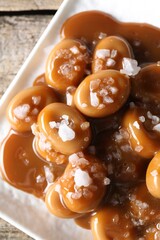 Tasty candies, caramel sauce and salt on wooden table, top view