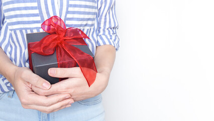 Young woman holding a black gift box with a red ribbon in her hands. Isolated on white background.
