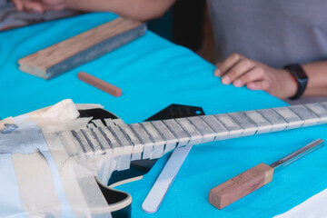 Black electric guitar in repair shop with the hands of a guitar luthier fixing it, frets alignment.